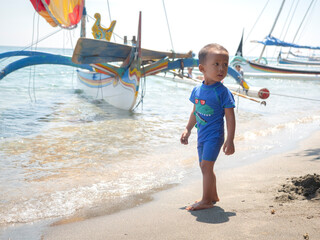 Asian toddler boy standing on the sand of a beach boat with an ocean and traditional background....