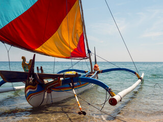 Close up of a traditional Indonesian sailing boat docked on a white sandy beach with a clear sea...