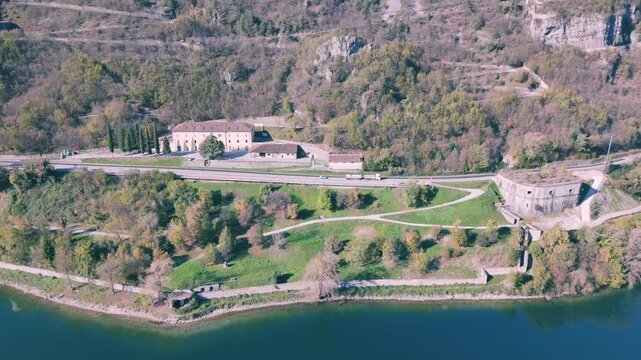 Aerial shot of Lake Idro in front of Rocca d'Anfo which is nestled on forested mountain with a road