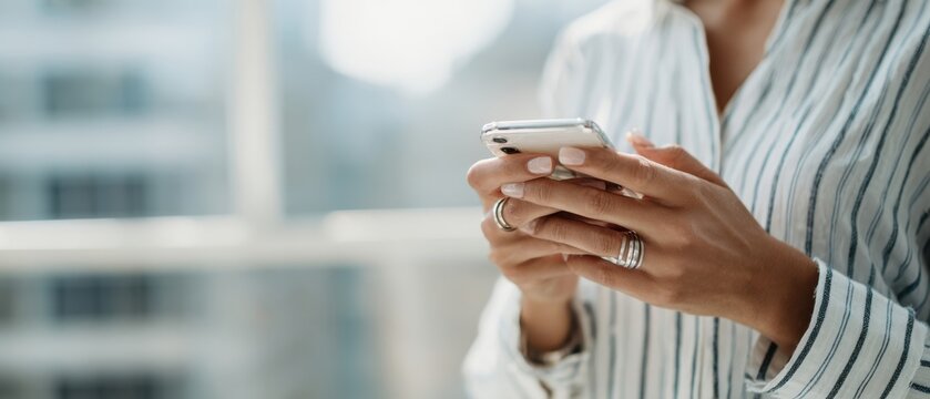 The woman using a smartphone while sitting by a bright window.