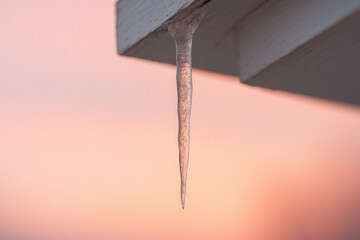 Delicate Icicle Hanging from Wooden Roof Edge with Warm Pink Winter Sunset Sky in Background