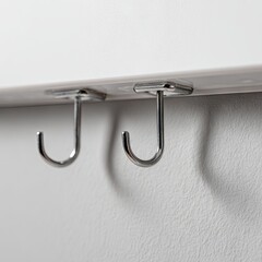 Two small, chrome J-hooks affixed to a white surface with square bases