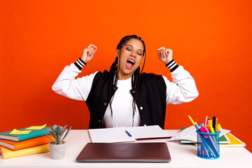 Teenage student stretching and yawning at her desk while studying with notebooks and supplies on...