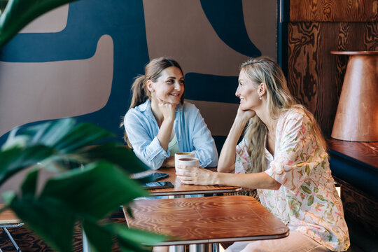 Two pretty caucasian women are talking while sitting in a cafe.