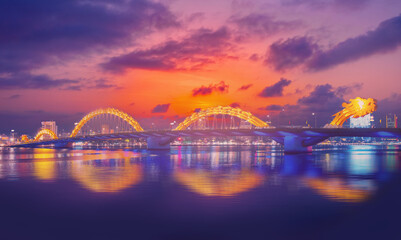 Naklejka premium Dragon bridge at night in Da Nang Vietnam, illuminated architecture and scenic reflections