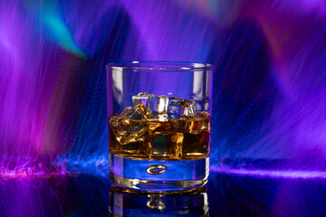 Glass of whiskey with ice on purple background