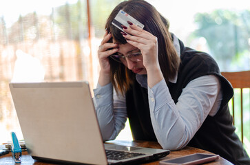 Sad Young Woman In Front Of Laptop Holding A Credit Card And Holding Her Head Worriedly