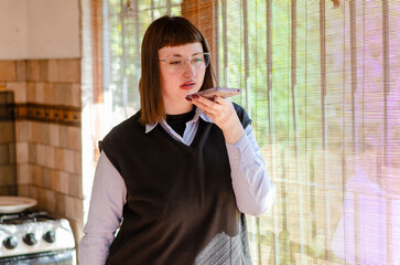 Serious young female employee or student wearing glasses sending audio message with a mobile phone