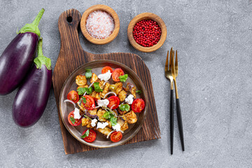  Georgian salad with deep fried eggplant, tomatoes, onions, feta cheese and cilantro on grey background. Vegetarian food with eggplant and other vegetables, top view