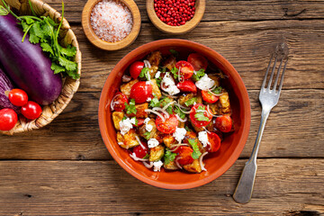  Georgian salad with deep fried eggplant, tomatoes, onions, feta cheese and cilantro. Vegetarian food with eggplant and other vegetables, wooden background top view