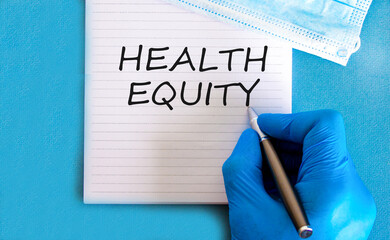 Health equity symbol. Concept words Health equity on beautiful white note. Doctor's hand in blue...