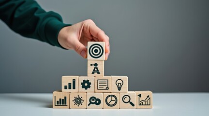 Business Goal Setting - A hand placing a wooden block with a target icon on a pyramid of business icons, symbolizing strategic planning and growth