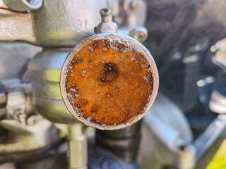 A rusty bolt is sitting on a metal surface. The bolt is old and worn, with a brownish-orange color. The surface it is sitting on is also old and worn, with a rusted appearance