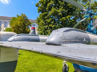 A grey and red plane is sitting on a grassy field. The plane is old and has a red light on the side. The scene is peaceful and calm, with the grass and trees providing a natural backdrop for the plane