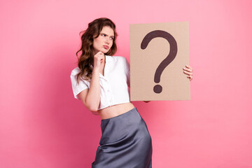 Young woman in smart casual attire posing with a large question mark sign against a pink background...