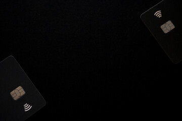 Two black chip-enabled payment cards, placed against a dark black background with copy space in the...