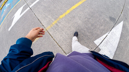 A downward view of a person walking on a concrete surface, featuring road markings, directional arrows, and lines, portraying motion, perspective, and casual outdoor activity with a unique composition