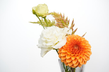 Small floral arrangment of orange and white flowers in a glass vase. White background. Dahlia, lisianthus, and celosia flowers.
