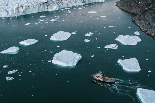 Aerial view of a boat by a bay with icebergs and a glacier