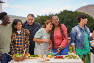 Elderly multiracial women having fun together during barbecue food preparation at home rooftop -...