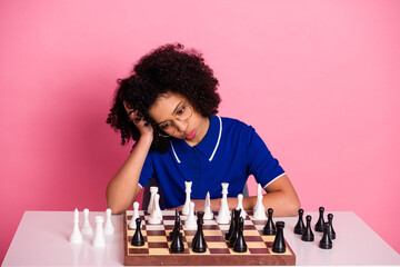 Sad thoughtful young woman strategizing during a chess game against a vibrant pink background