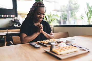 Joyful Black woman smiles while praying before meal, expressing gratitude, mindfulness, and balance...
