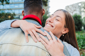 Joyful multiracial Couple Sharing Tender Outdoor Embrace as Young Woman with Radiant Smile Hugs Her Boyfriend in Park Two people embracing each other. Emotional union and relationship. High quality