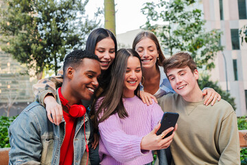 A happy group of friends sharing laughter and excitement as they watch something entertaining on their smartphone. This engaging moment captures the essence of youth and connection among friends.