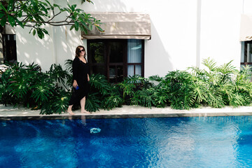 Middle-aged woman walking barefoot near pool with smartphone, expressing digital mobility, relaxed...