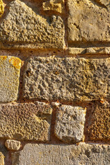Close-up view of rough textured stone wall blocks in warm sunlight, showing weathered surface details