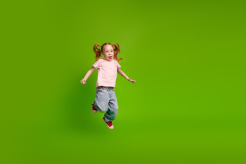 Excited young schoolgirl jumping with energy on vibrant green background wearing casual outfit