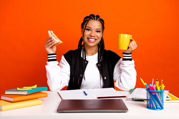 Cheerful young student enjoying a snack and coffee at a school desk, expressing positivity and...