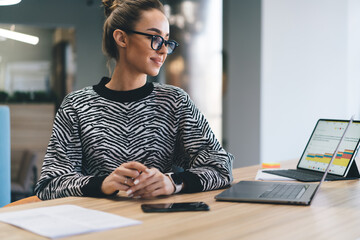 Freelancer in zebra sweater glancing sideways, sitting at modern wooden table with tech devices,...