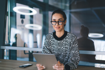 Smiling freelancer with tablet in stylish dark office, expressing friendly mood, tech literacy and...