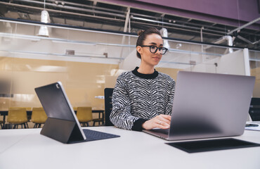 Focused businesswoman in zebra-print sweater working on laptop in modern open office, representing concentration, productivity, and digital competence in creative tech environment.