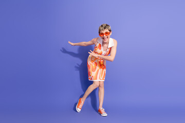 Energetic young woman in retro inspired summer dress posing playfully against vibrant purple background