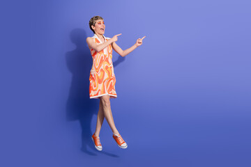 Joyful young woman pointing in excitement while wearing a vibrant patterned dress against a...