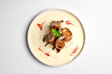 Top view of crispy fried banana spring rolls served with ice cream sauce, chocolate drizzle, and strawberry syrup on a white plate over white background.