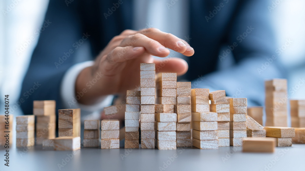 Aufkleber hand placing wooden blocks on a table building a tower with a suit in the background in a blurred vi