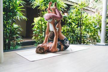 Young woman balancing playful child on feet during home yoga routine, demonstrating trust, core strength and active parenting in vibrant and healthy lifestyle.