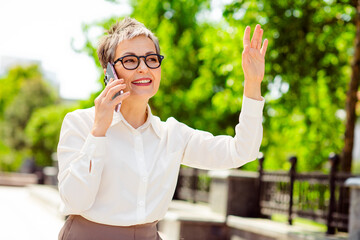 Confident professional woman in bright setting using mobile phone and greeting while wearing sleek...