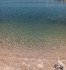Seeufer mit Kiesel und klarem, frischem Wasser von oben, bis ins tiefe, blaue Wasser, Teich im Urlaub