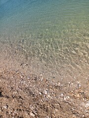 Seeufer mit Kiesel und klarem, frischem Wasser von oben, Teich im Urlaub