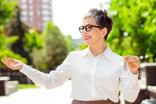Mature businesswoman holding keys outdoors in an urban environment displaying professionalism and charm