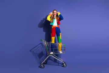 Vibrant young woman posing stylishly in a colorful denim outfit while standing in a shopping cart...