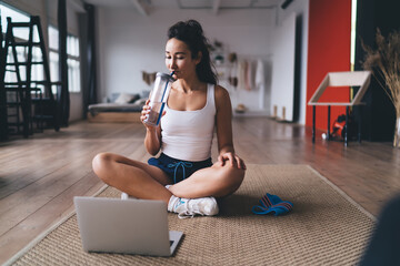 Woman hydrates during tech-guided home workout, showing balance of physical training and mindful...