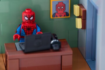 Naklejka premium Tambov, Russian Federation - February 12, 2025 Lego Spider-Man minifigure working behind a black laptop on workplace at the office