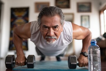 Determined older man doing push-ups with dumbbells on an exercise mat
