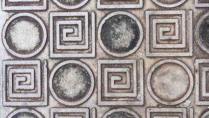 Close-up of a textured concrete surface with repeating circular and square spiral patterns.