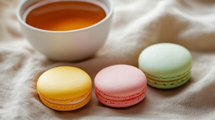 Obraz premium flat lay of macarons in bright, cheerful colors like pink, yellow, and mint green, arranged elegantly on a textured linen cloth with tea in the background